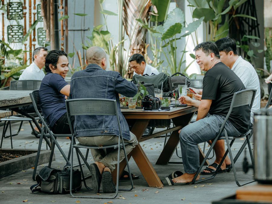Grupo de amigos rindo e conversando ao redor de uma mesa em um café ao ar livre